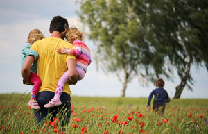 A father with two children in his arms walking through a meadow